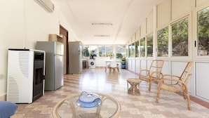 Amplia sala de estar con cocina, ventanas grandes y zona de descanso con sillas de mimbre.