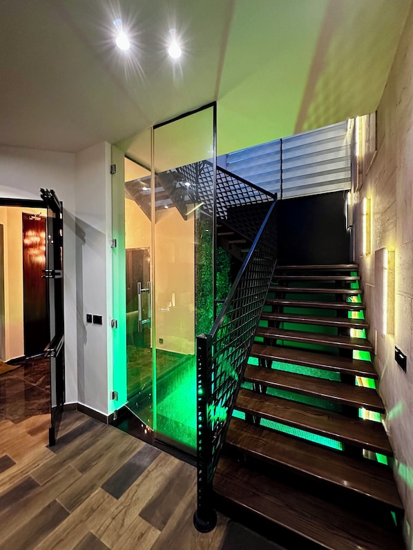 Una escalera moderna con iluminación LED verde, un panel de vidrio y suelo de madera.