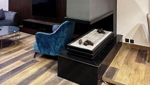 Una sala moderna con un televisor de pantalla plana, un sillón azul, una mesa de centro negra y una chimenea con una toalla amarilla.