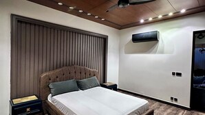 Un dormitorio moderno con una cama grande, un ventilador de techo, un equipo de aire acondicionado y una mesita de noche.
