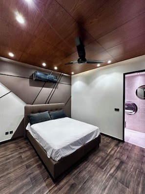 Un dormitorio moderno con cama, ventilador de techo, iluminación empotrada y techo de madera.