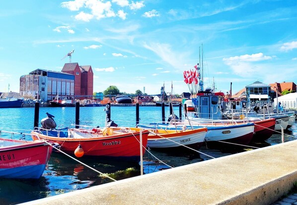 Un port où des bateaux sont amarrés, un bâtiment à la façade rouge et un ciel bleu clair.