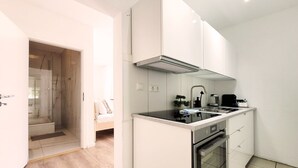 A compact kitchen with white cabinets, a black countertop, a built-in oven, and a small dining area with a bench. - Charming apartment by the harbor with free bed linen package and terrace - (Neustadt in Holstein)
