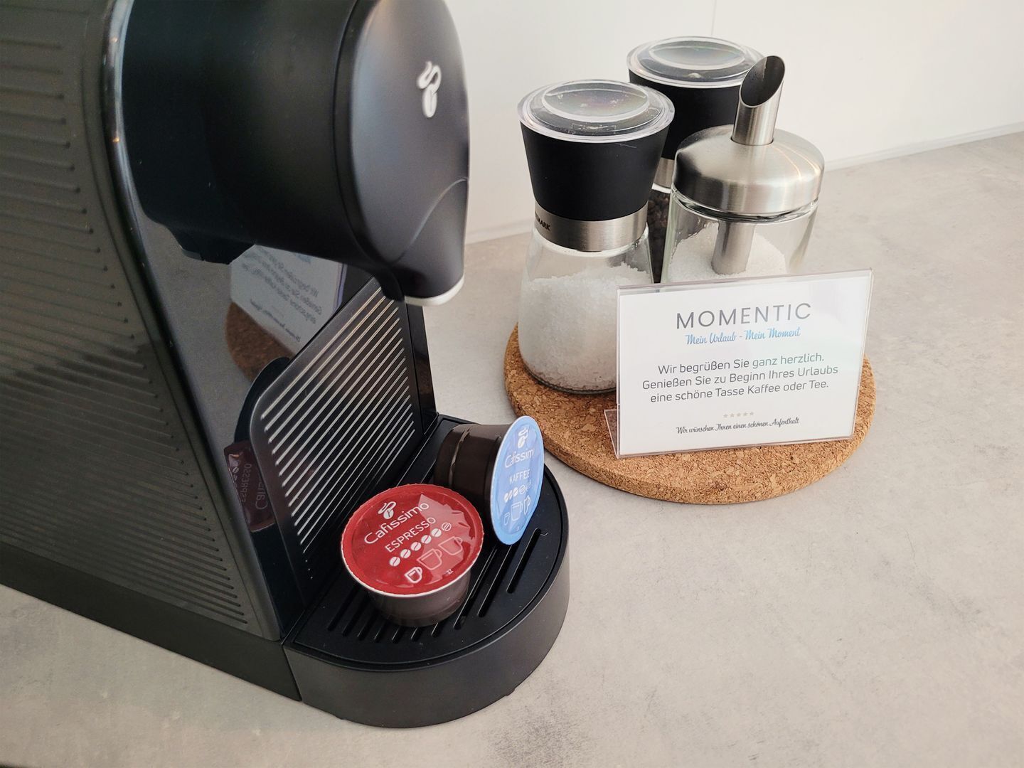 A coffee machine with a drip tray, a coffee pod, and a sign with the word "MOMENTIC".