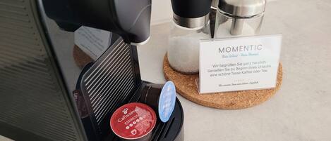 A coffee machine with a drip tray, a coffee pod, and a sign with the word "MOMENTIC".