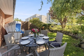 A patio with wicker furniture, a round table set for four, and a flower vase. - Mattis Hüs - Quietly situated semi-detached house Mattis Hüs. With garden and (Sylt)