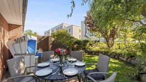 A patio with wicker furniture, a round table set for four, and a flower vase. - Mattis Hüs - Quietly situated semi-detached house Mattis Hüs. With garden and (Sylt)