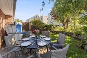 Eine Terrasse mit Korbmöbeln, einem runden Tisch für vier Personen und einer Blumenvase.