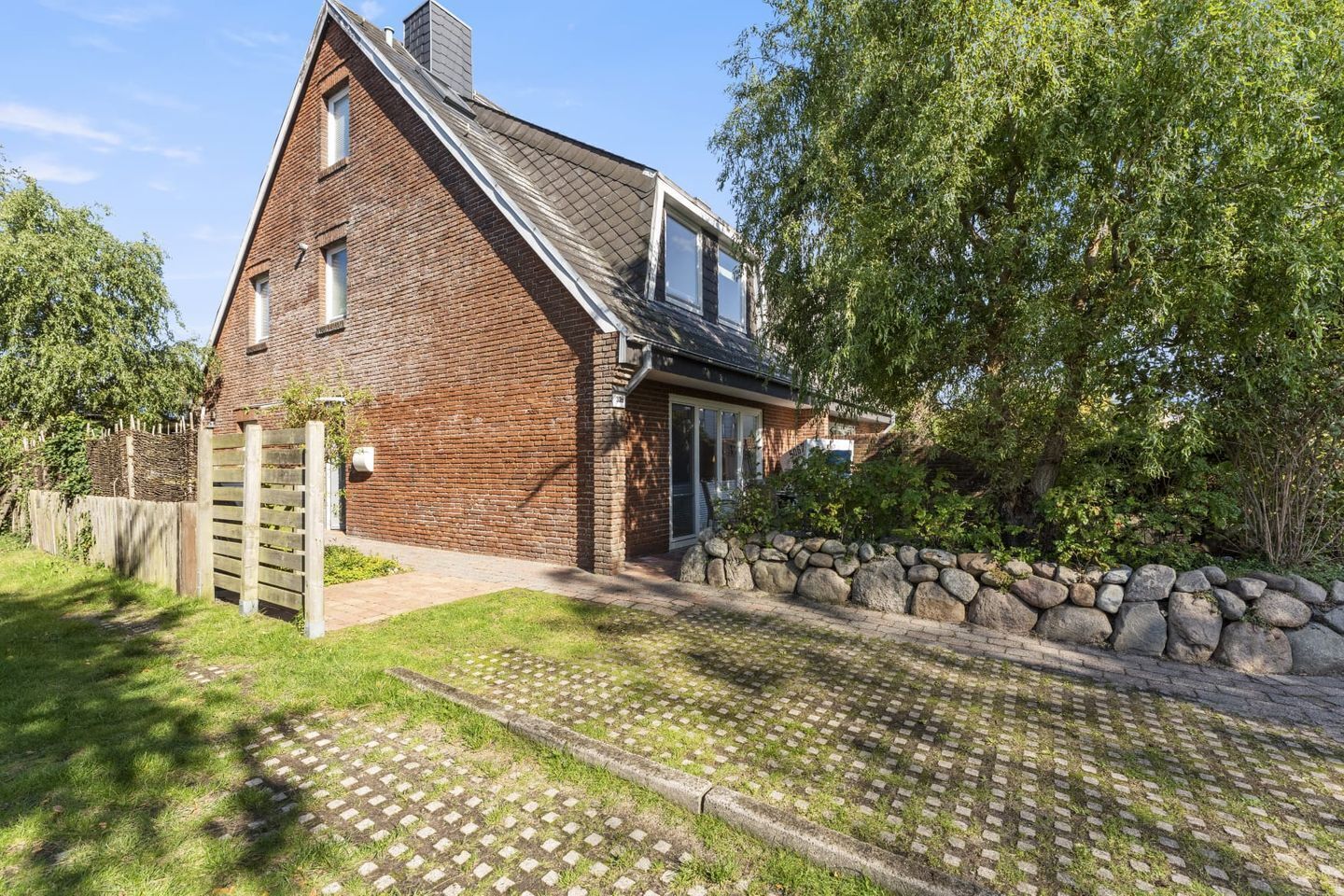 Een bakstenen huis met een stenen muur, een houten hek en een geplaveid pad.