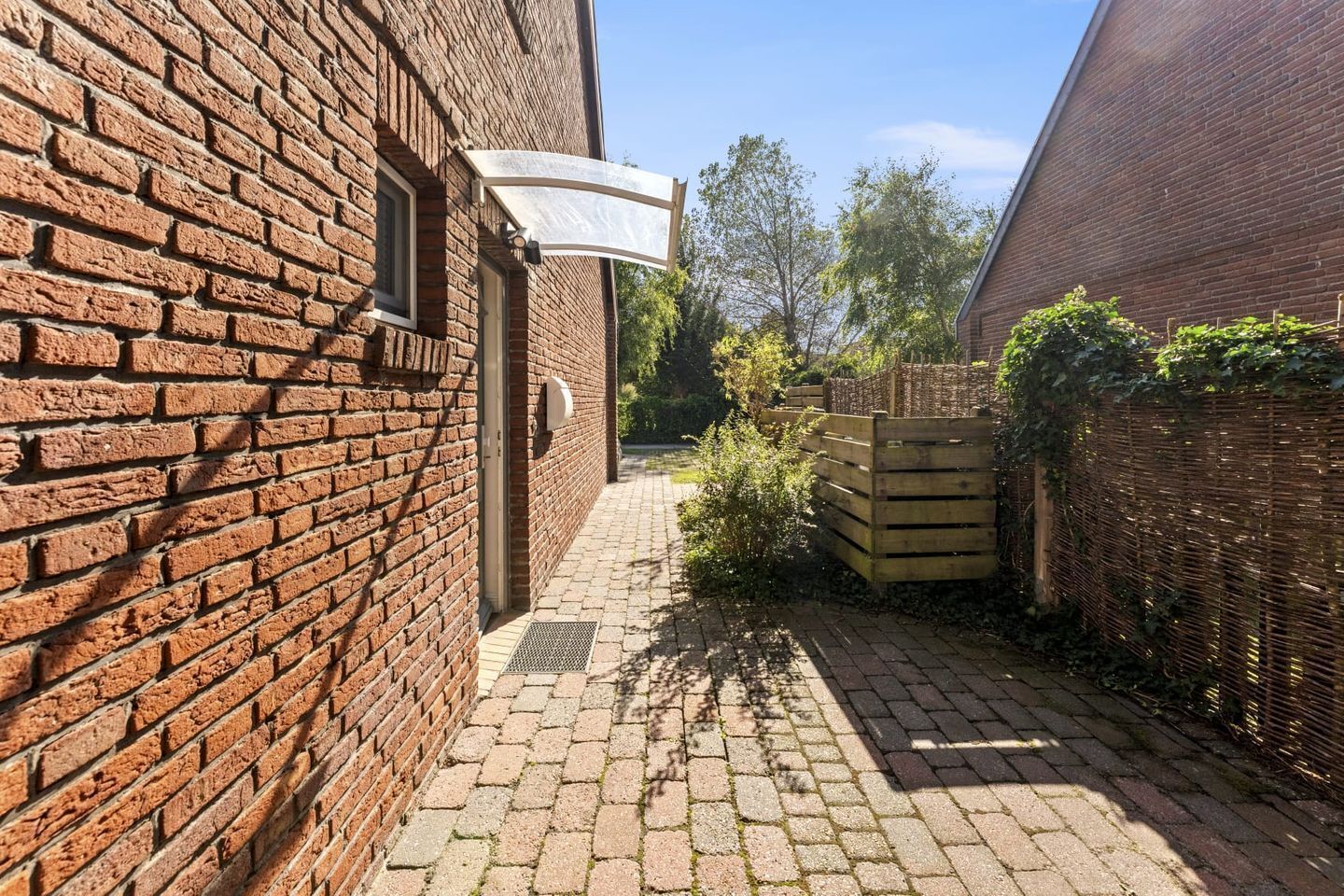 Een smalle steeg met een houten poort, een wit zonnescherm en een bakstenen gebouw aan de linkerkant.