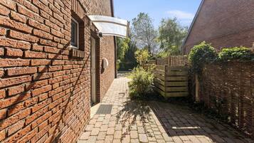 Een smalle steeg met een houten poort, een wit zonnescherm en een bakstenen gebouw aan de linkerkant.