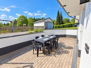 Eine Terrasse im Freien mit einem Esstisch, umgeben von einer weißen Mauer und einem Holzzaun.