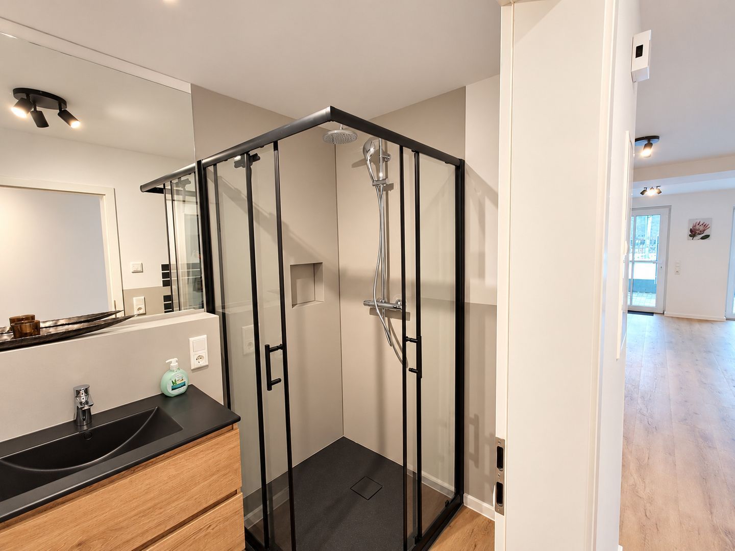 A modern bathroom with a glass shower enclosure, a black countertop, and a wooden vanity.