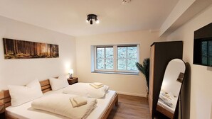 Un dormitorio con cama, mesitas de noche, ventana, un cuadro y espejo.