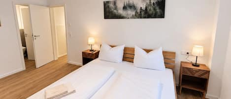 Ein Doppelbett mit zwei Nachttischen, ein Gemälde darüber und ein Holzboden.
