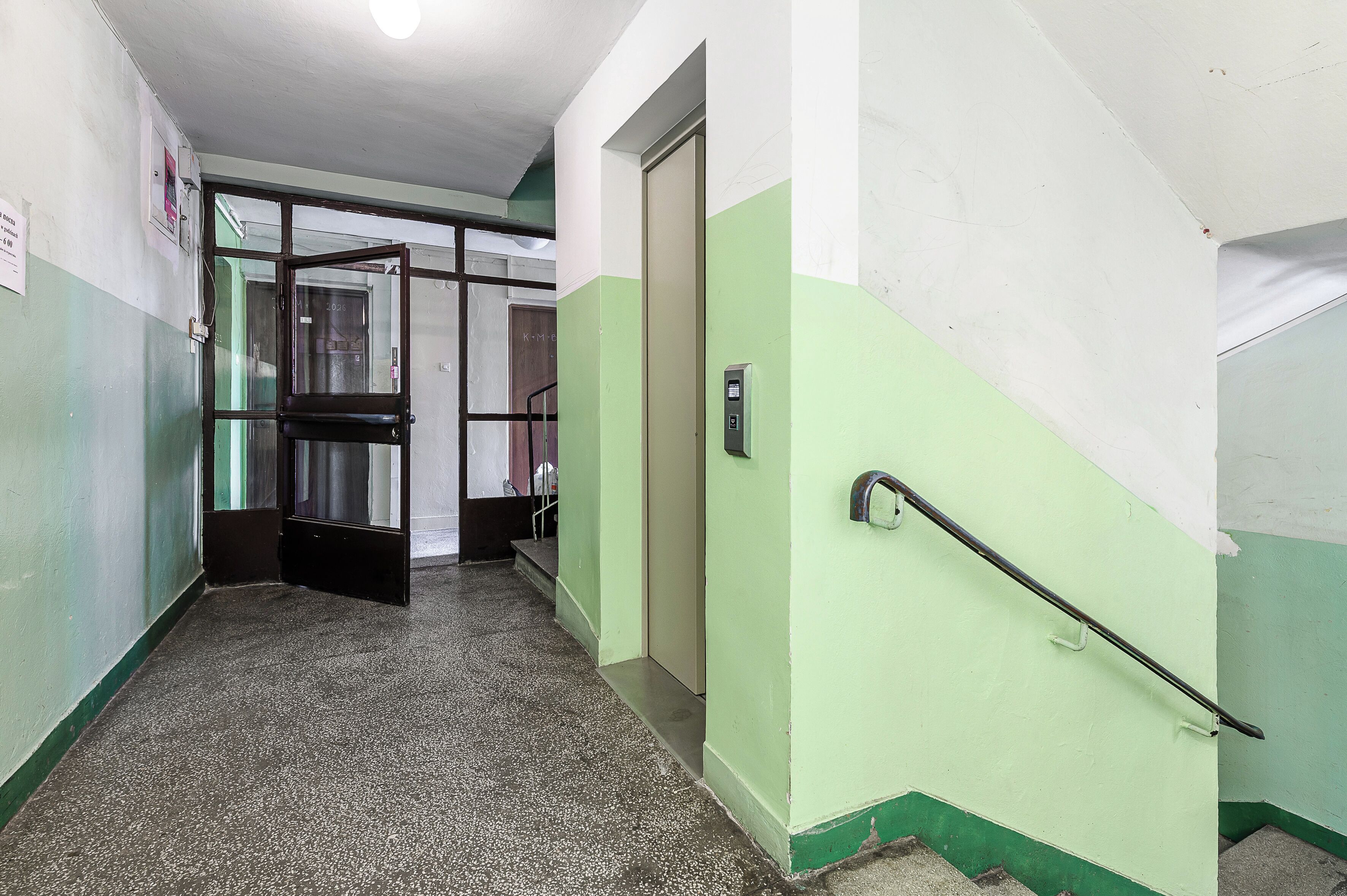 A hallway with a green and white wall, a door, a handrail, and a staircase.