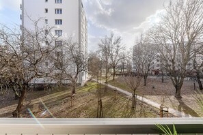 A view of a park with bare trees and a pathway, a white building in the background, and a clear sky. - Lumina apart with balcony in Warsaw (Warsaw)