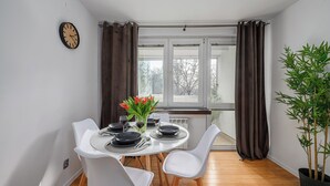 A dining area with a round table, white chairs, a clock on the wall, and a window with curtains. - Lumina apart with balcony in Warsaw (Warsaw)