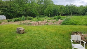 Un'area verde all'aperto con una sedia bianca, un grosso masso e un'aiuola con piante.