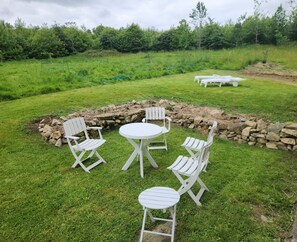 A grassy outdoor area with a stone wall, white chairs, and a table.