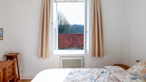 Una camera da letto con un letto, una finestra con tende, un termosifone e un comò.