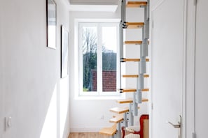 A narrow stairway with a wooden handrail and a red chair at the bottom.