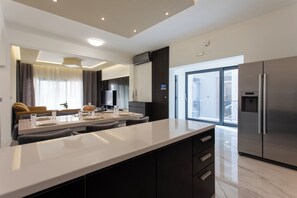 A modern kitchen with a large island, dark cabinetry, and a stainless steel refrigerator. - Ocean Luxe Apartment (Split)