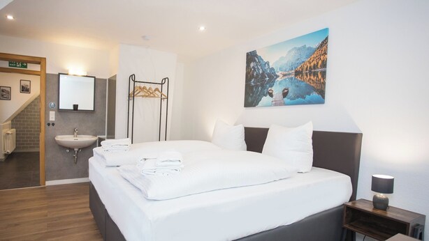 A modern hotel room with a large bed, a bedside table with a lamp, a bathroom with a sink and mirror, and a staircase leading to an upper floor. - The perfect vacation home for families in Winterberg for up to 20 people - with plenty of space, comfort and a cozy terrace (Winterberg)
