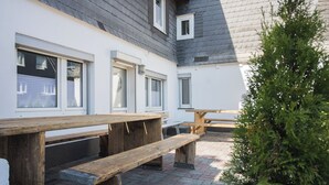 A courtyard with wooden benches and tables, a small tree, and a building with windows and a door. - The perfect vacation home for families in Winterberg for up to 20 people - with plenty of space, comfort and a cozy terrace (Winterberg)