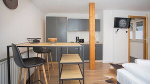 A compact room with a bed, a small dining area with a table and chairs, a kitchenette, and a television on the wall. - The perfect vacation home for families in Winterberg for up to 20 people - with plenty of space, comfort and a cozy terrace (Winterberg)