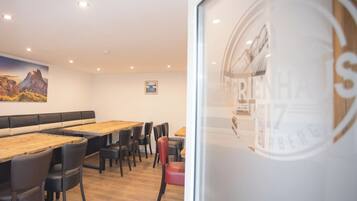Een restaurantinterieur met houten tafels, zwarte en rode stoelen en een schilderij van een berglandschap aan de muur.
