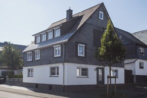 A two-story residential building with a dark roof, white walls, and multiple windows. - The perfect vacation home for families in Winterberg for up to 20 people - with plenty of space, comfort and a cozy terrace (Winterberg)