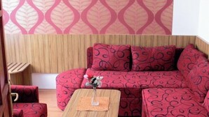 Ein Zimmer mit Holzboden, einem rot gemusterten Sofa, einem Holztisch und einer Wand mit Muster.