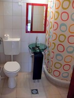 Uma casa de banho com sanita, lavatório de vidro, espelho e cortina de chuveiro com padrão de bolinhas.