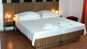 A hotel room with a large bed, wooden headboard, two bedside lamps, and a red chair. - Hid Hotel (Budapest)