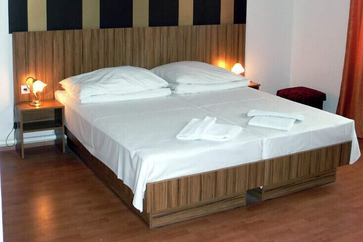 A hotel room with a large bed, wooden headboard, two bedside lamps, and a red chair.