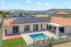 Une maison moderne dotée d’une piscine, de panneaux solaires et d’une terrasse clôturée.