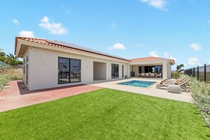 A modern house with a swimming pool, a patio, and a fenced garden.