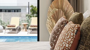 Ein Hotelzimmer mit Bett, Blick auf einen Swimmingpool und einem Balkon mit Stühlen und Tisch.
