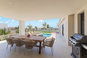 Une terrasse extérieure avec une table à manger, des chaises, un barbecue et une piscine.