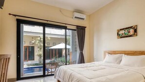 A hotel room with a large bed, a sliding glass door leading to a balcony with a pool, and a framed picture on the wall. - Dhita Kubu Guest House (Kerobokan)