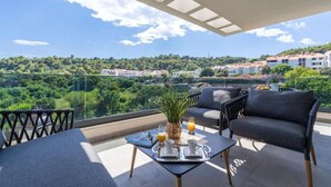 Een balkon met een tafel gedekt voor twee personen, een bank en uitzicht op een groen landschap met gebouwen in de verte.