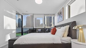 A modern bedroom with a large bed, a bedside lamp, and a city view through floor-to-ceiling windows. - Spacious 3BR on Bourke St Grand Balcony & City Views (Melbourne)
