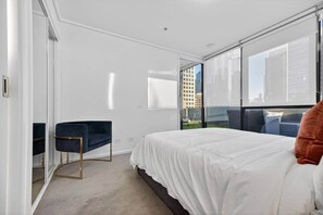 Une chambre d’hôtel moderne dotée d’un grand lit, d’un bureau et offrant une vue sur le paysage urbain grâce à de grandes fenêtres du sol au plafond.