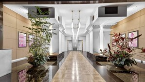 A modern hotel lobby with a polished floor, large potted plants, and a central staircase. - Spacious 3BR on Bourke St Grand Balcony & City Views (Melbourne)