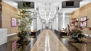 Un hall d’hôtel moderne avec un sol ciré, de grandes plantes en pot et un escalier central.