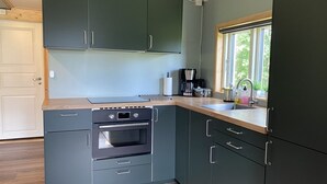 A compact kitchen with dark cabinets, a built-in oven, and a window with a view. - Villa Ragunda: Peace, space and Swedish adventure in the heart of Jämtland. (Hammarstrand)