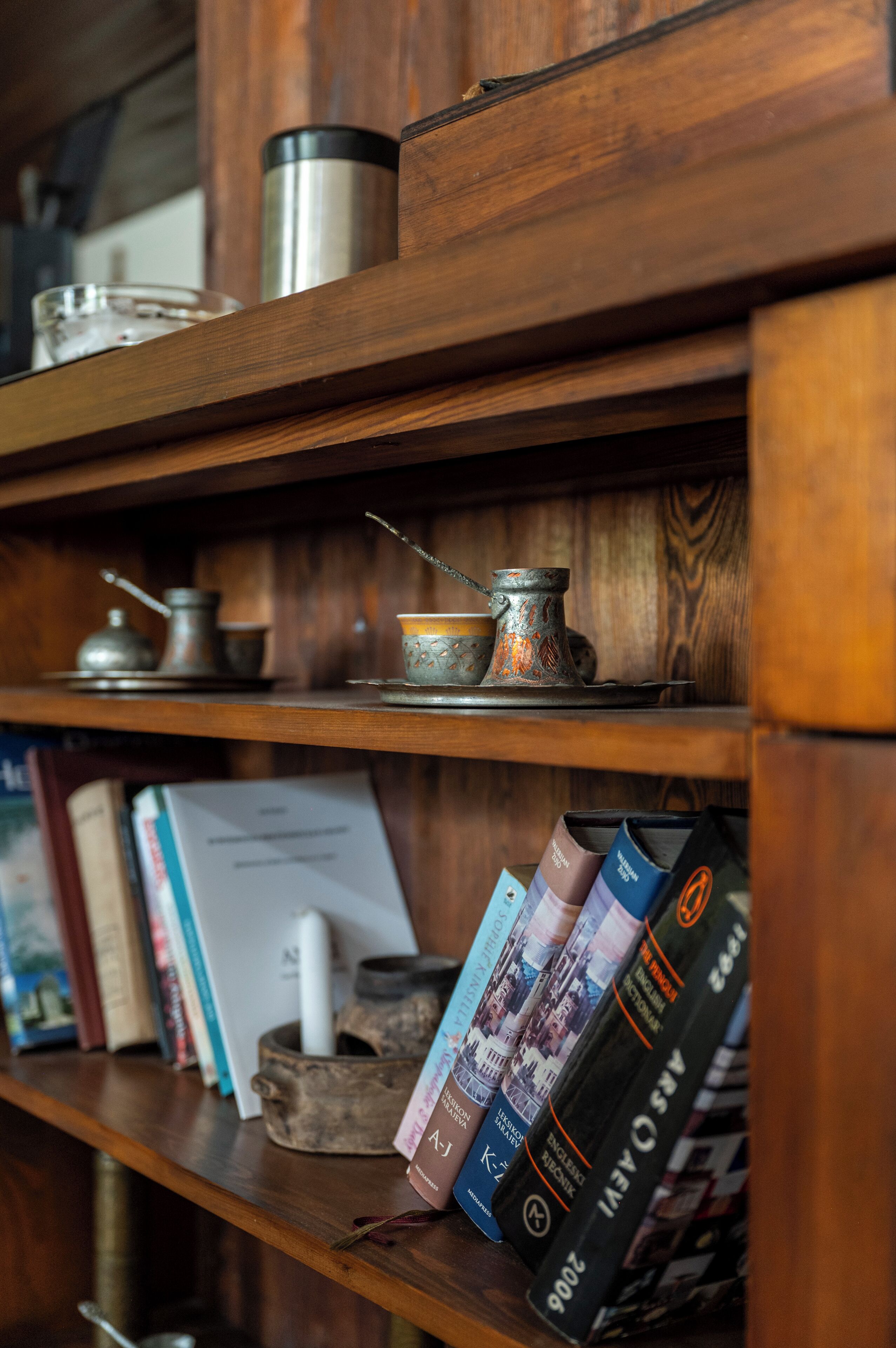A wooden shelf with books, a thermos, and a teapot.