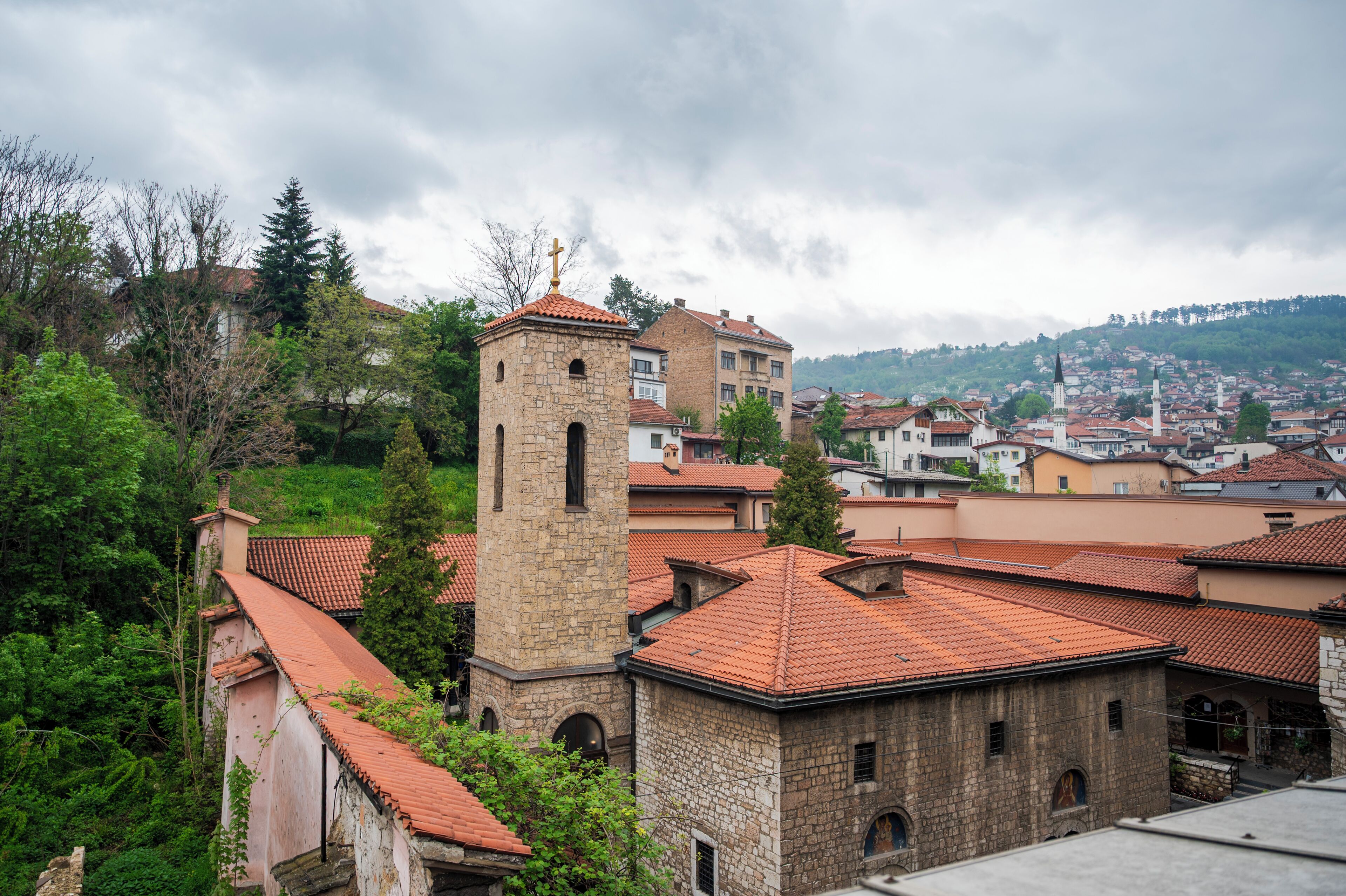 A historic stone building with a bell tower, surrounded by residential buildings with red-tiled roofs.