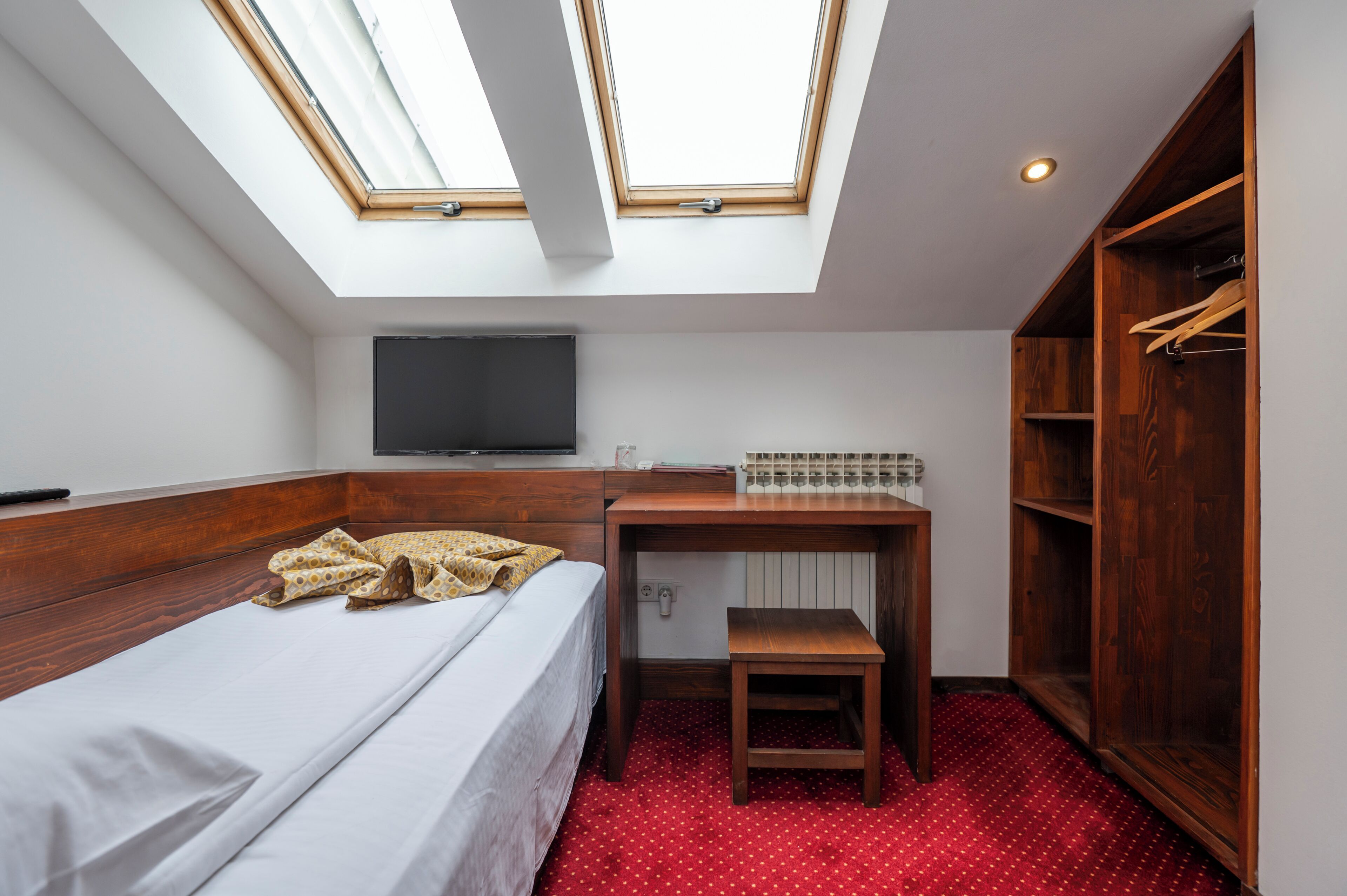 Une petite chambre comprenant un lit, un bureau, une télévision et une armoire.